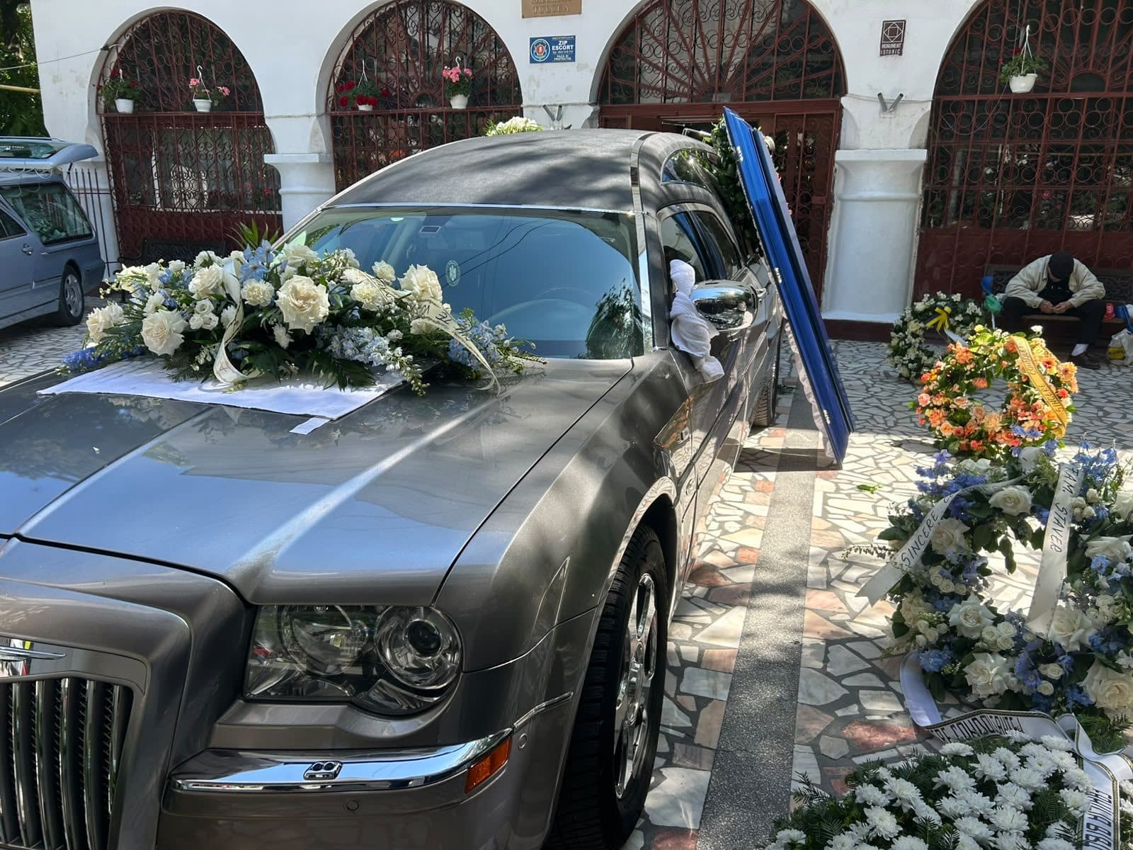 Autospeciala funerară cu aranjamente florale albe la biserică