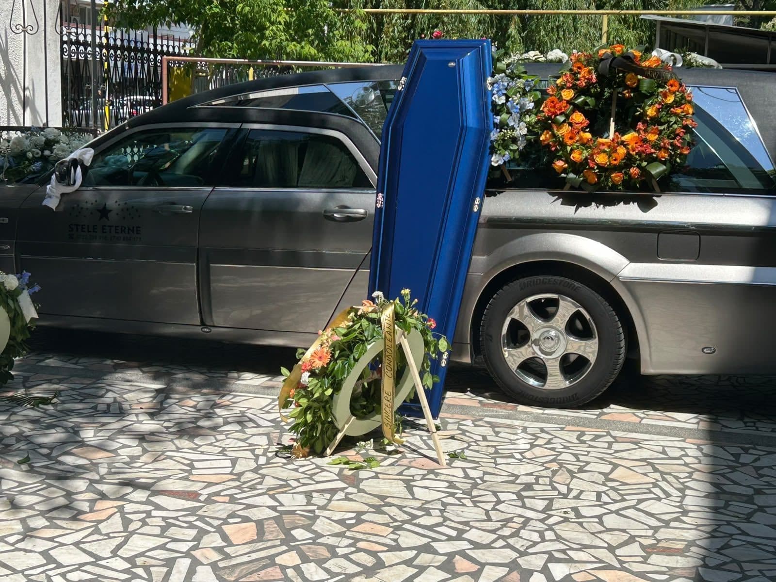 Sicriu albastru și coroană de flori lângă autospeciala funerară